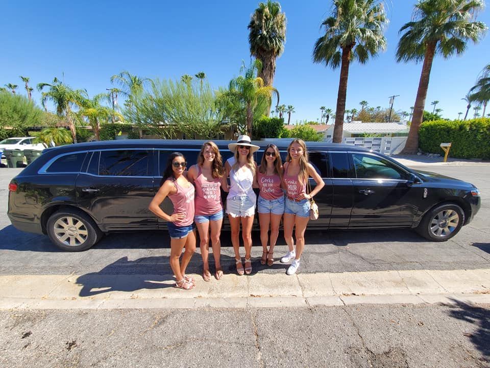 A group of women are standing in front of a limousine.