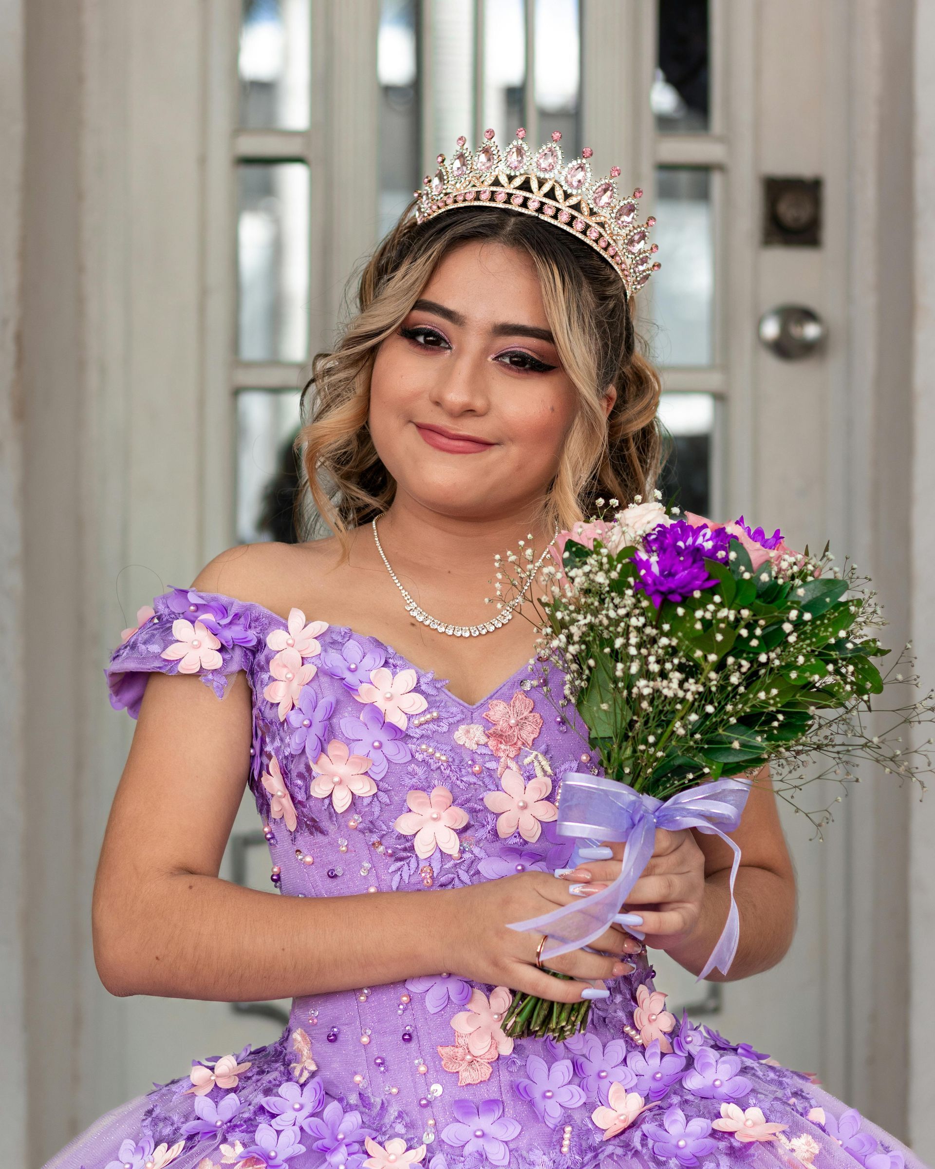 A woman in a purple dress and tiara is holding a bouquet of flowers.