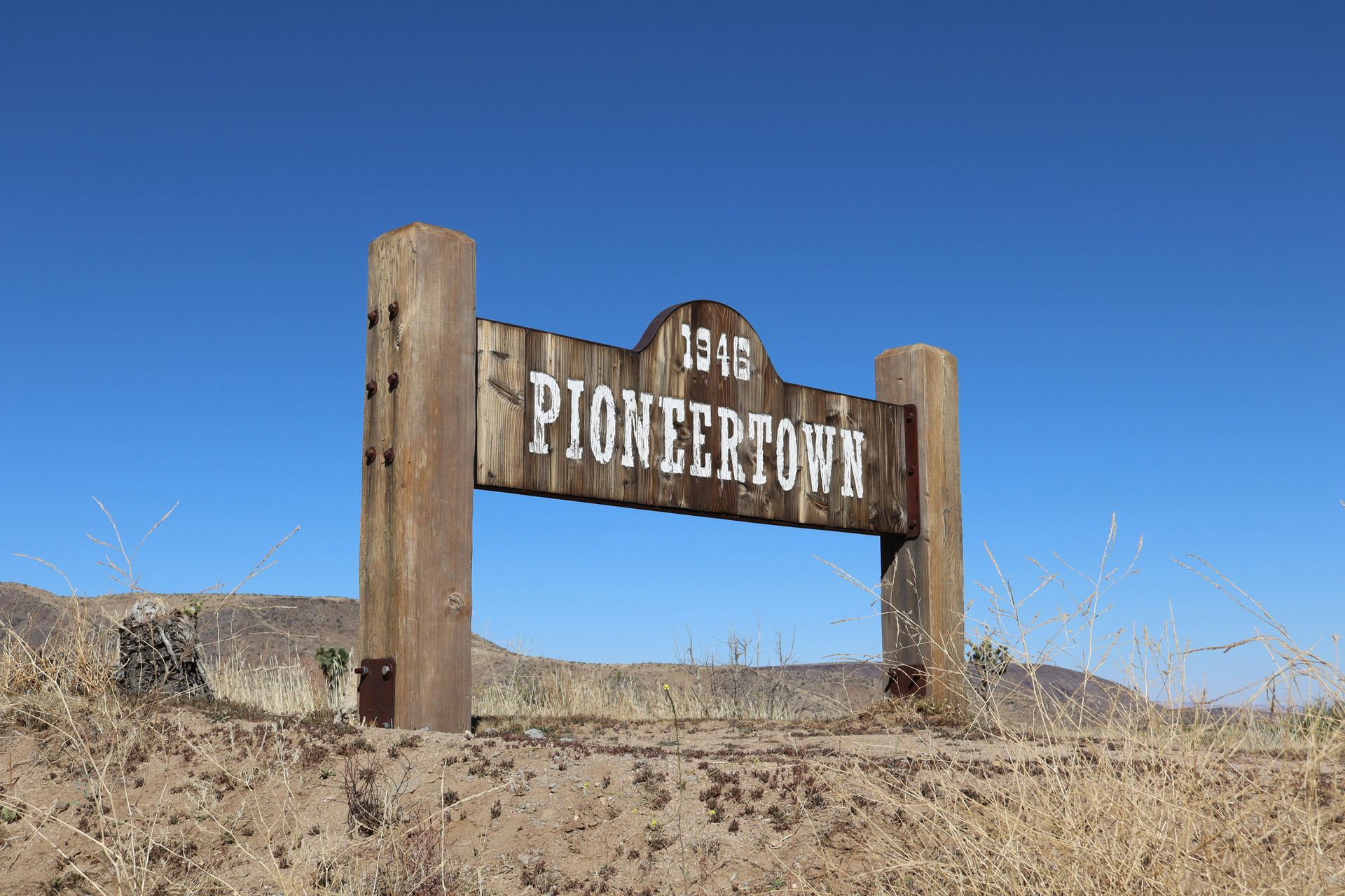 Pioneertown sign made of wood, set against a blue sky, in a desert landscape.