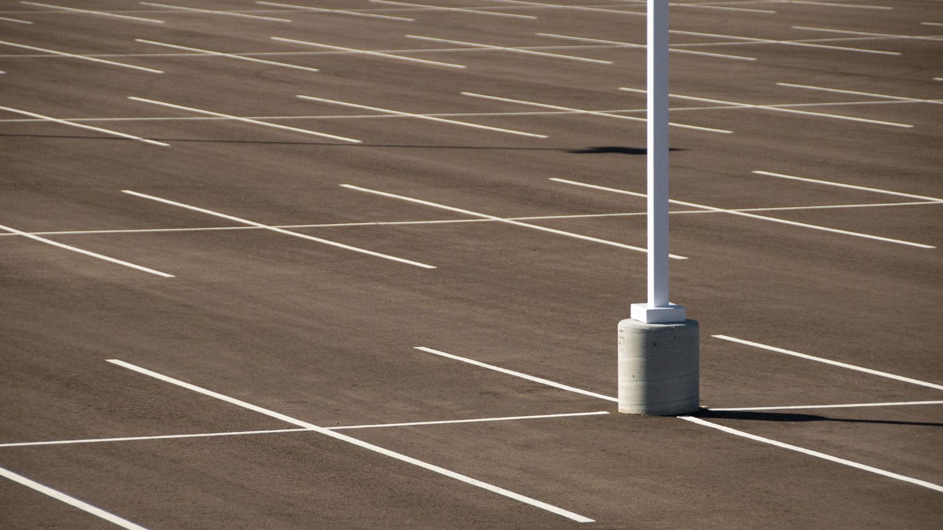 Empty parking lot with white lane markings and a lamppost base on asphalt