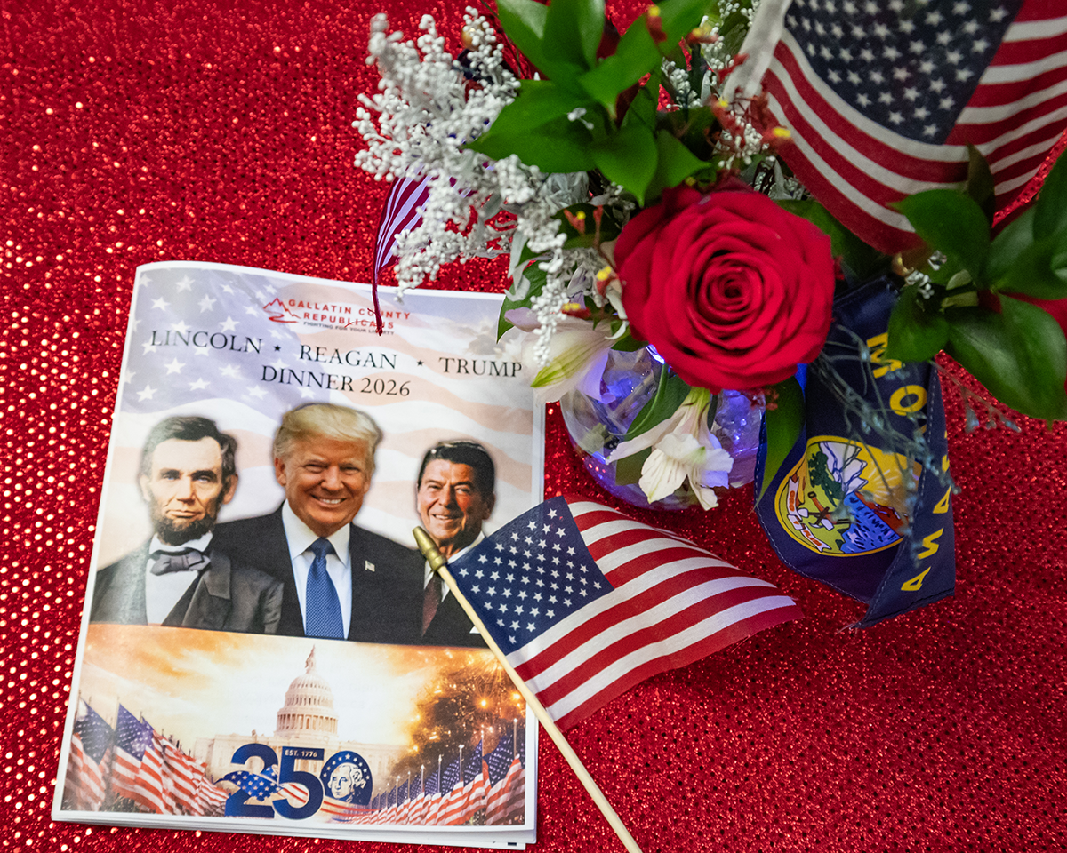 Patriotic display with U.S. flags, red rose, flowers, and a Trump commemorative card on a red glitter background