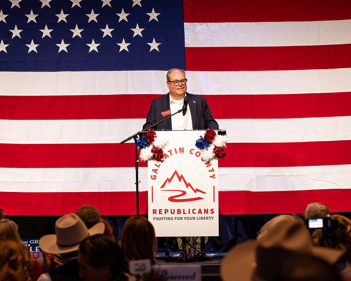 Speaker at podium before large American flag at a Republican event, with audience in foreground
