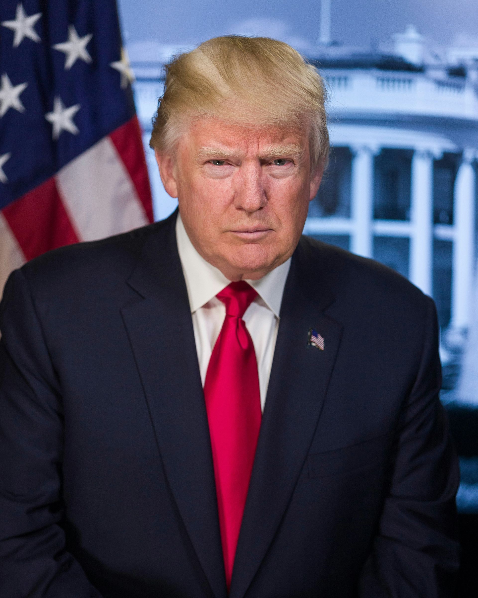 Man in dark suit and red tie standing in front of U.S. flag and White House backdrop