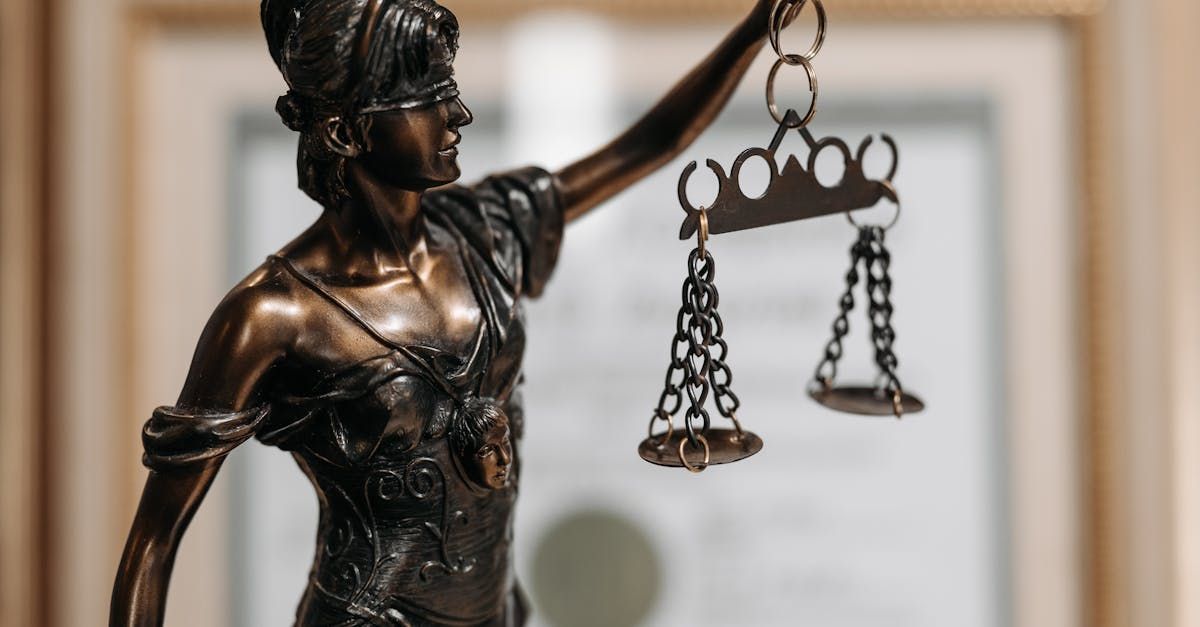Bronze Lady Justice statue holding scales, with a blurred courtroom-like background