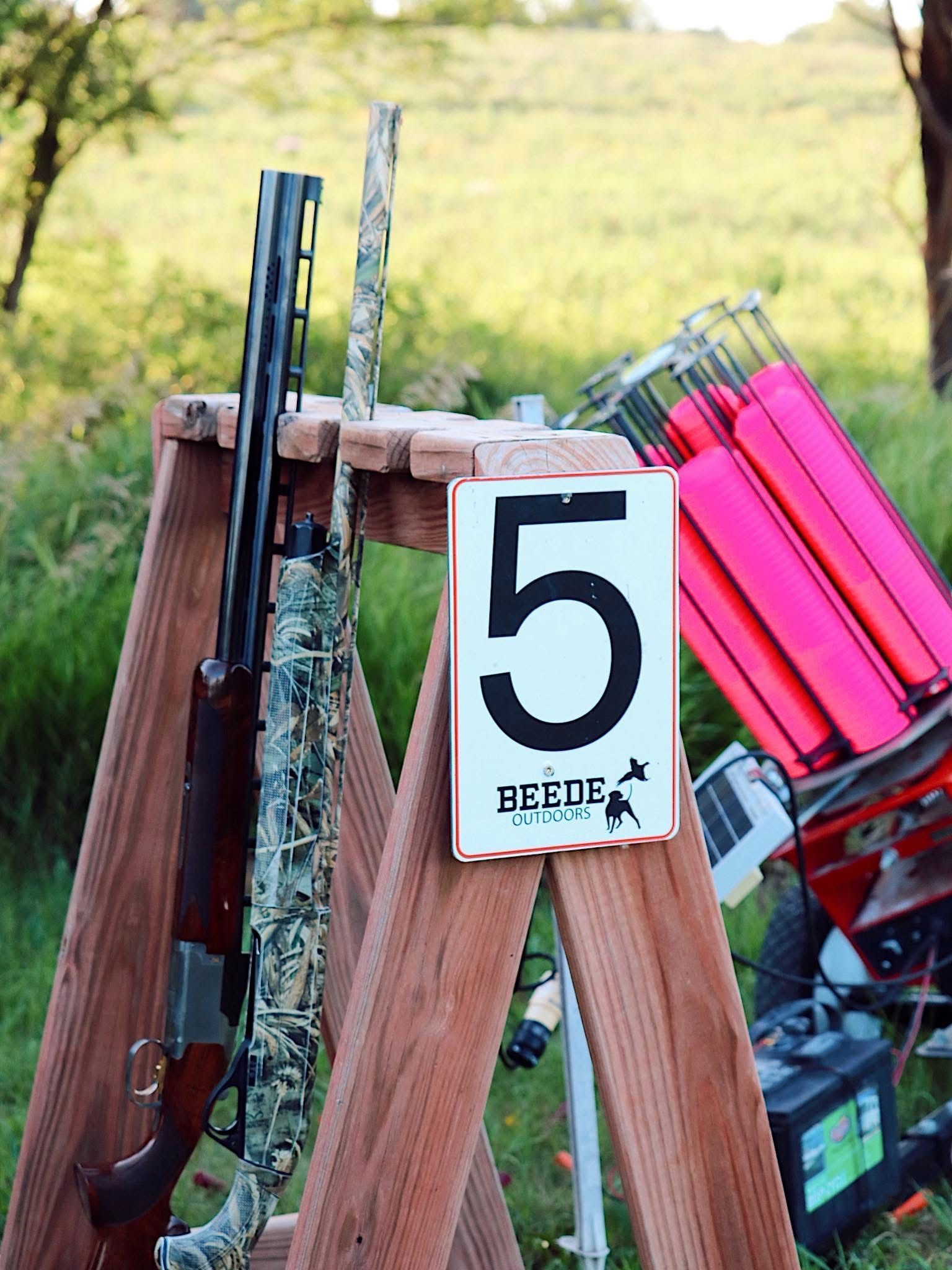 Shotgun on a wooden stand at station 5 of a shooting range, with pink clay targets.