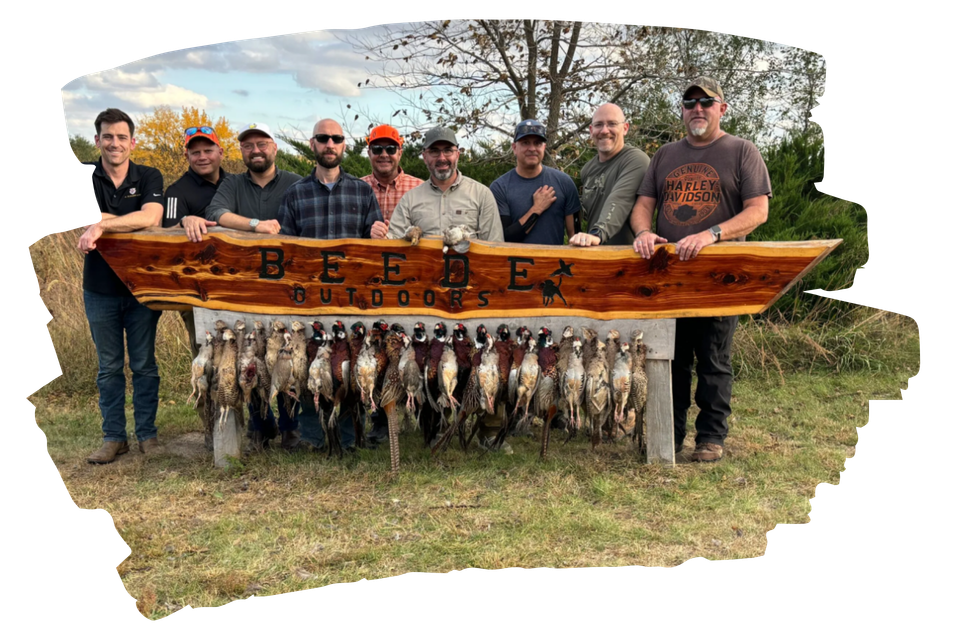 Group of men with hunted pheasants displayed on a wooden table. Outdoors on a grassy field.