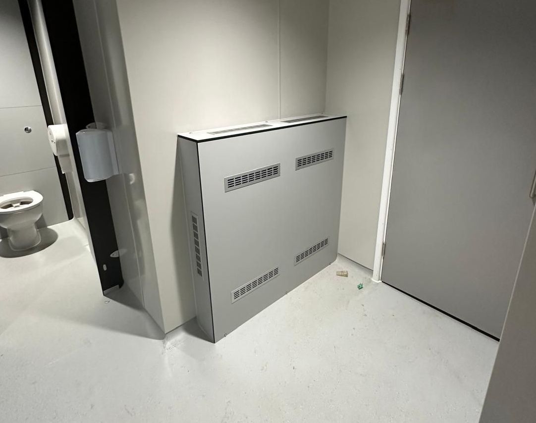 A white box is sitting in the corner of a bathroom next to a toilet.