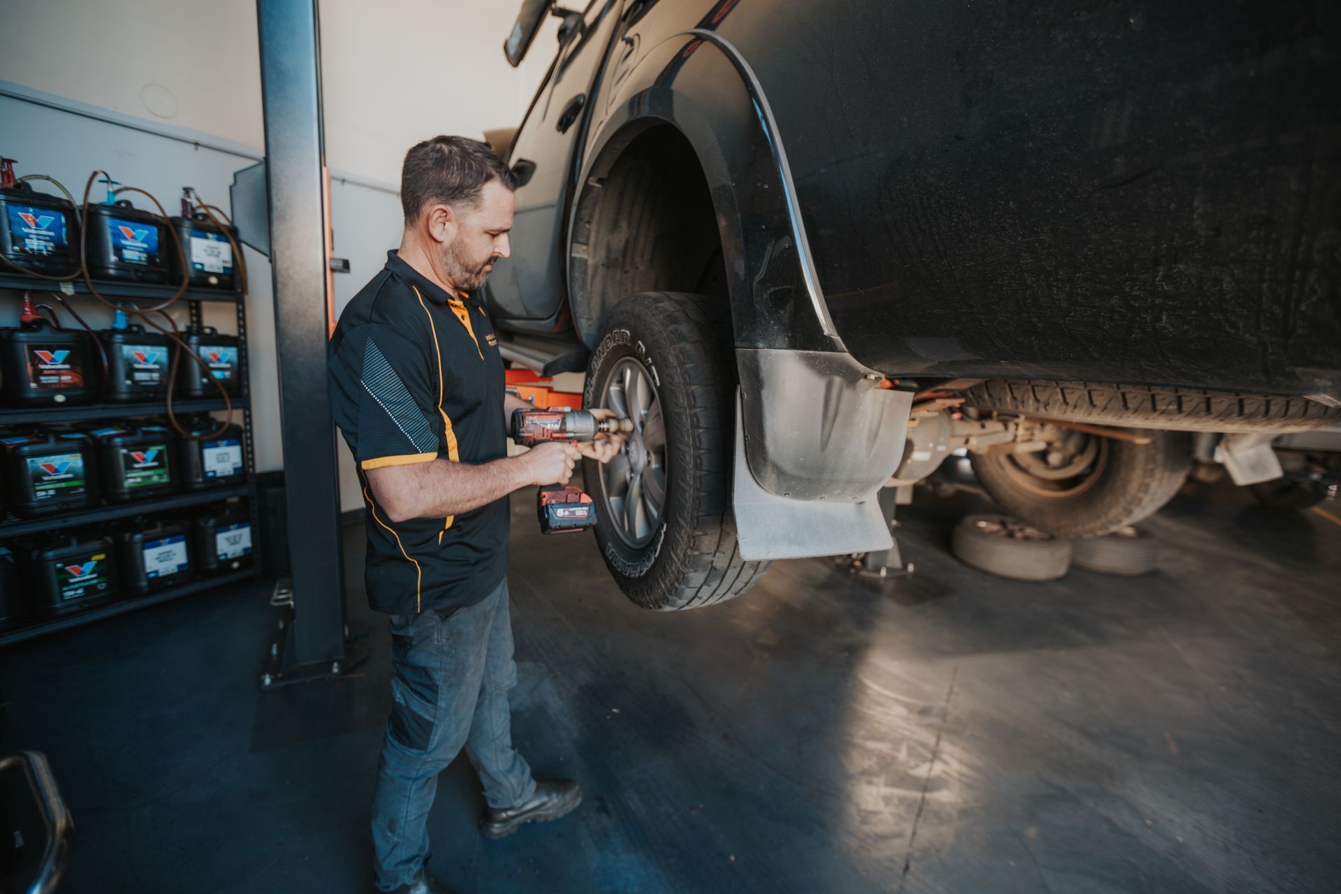 A Man is Holding a Piece of Metal Under a Car — Varsity Lakes Mechanical Repairs In Varsity Lakes, QLD