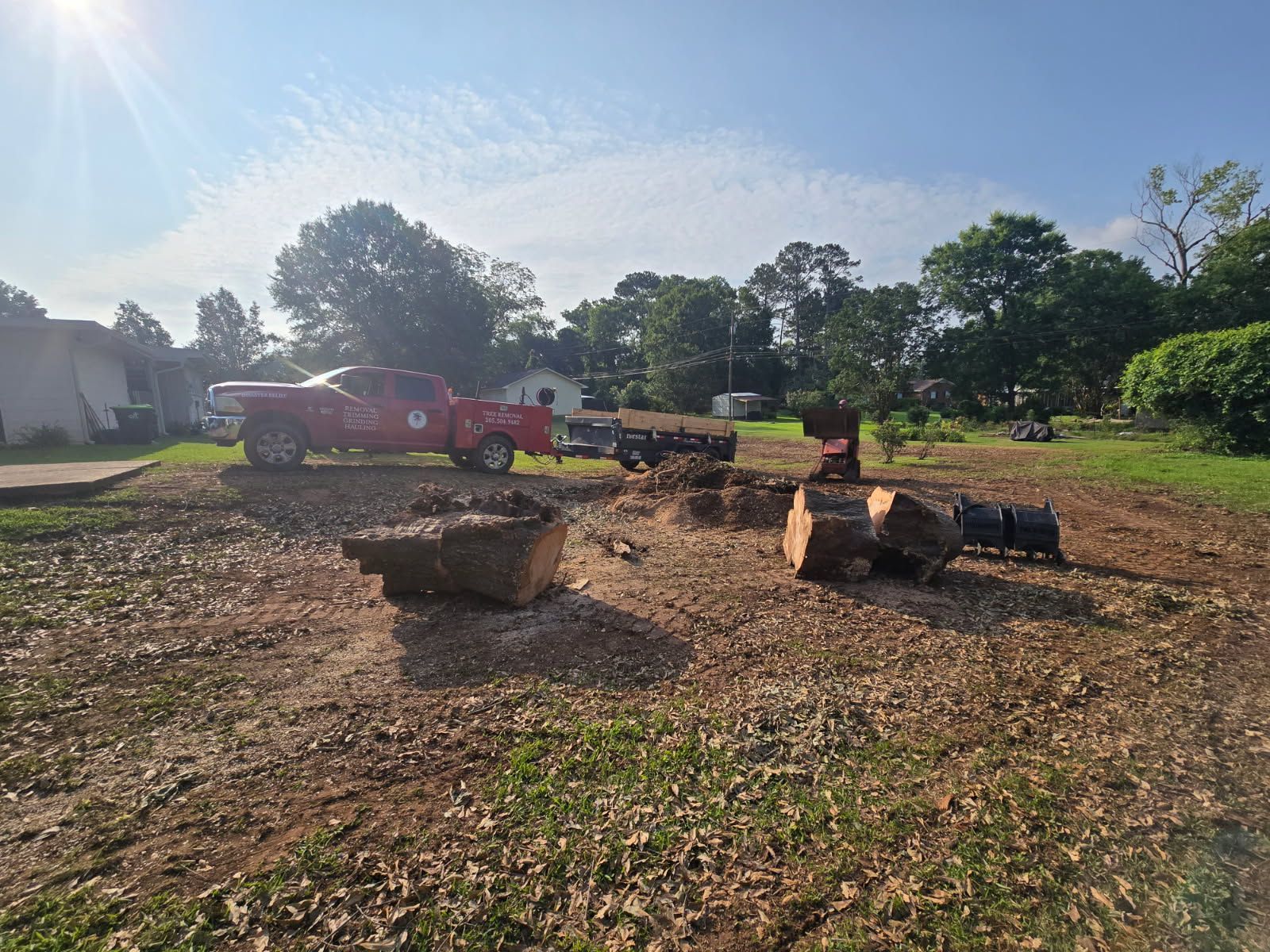 A red truck is driving down a dirt road next to a pile of logs.