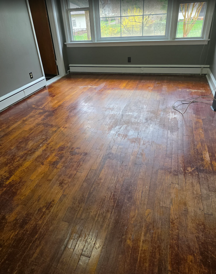 Empty room with worn hardwood floor, gray walls, and a large window