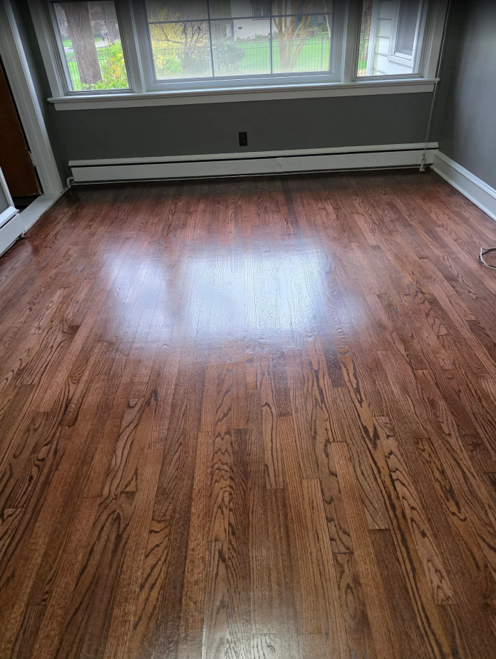 Empty room with glossy hardwood floor and large windows letting in natural light.