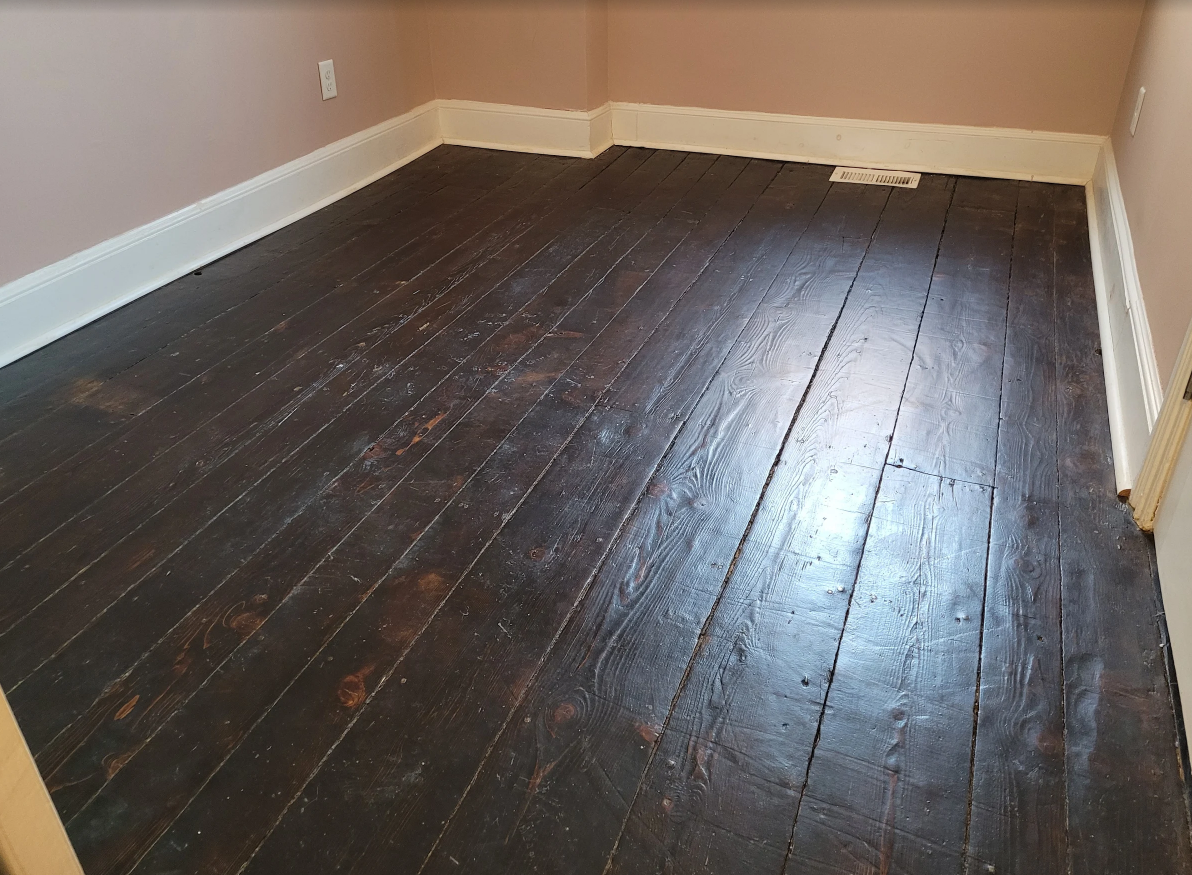 Empty room with dark hardwood floors, beige walls, and white baseboards