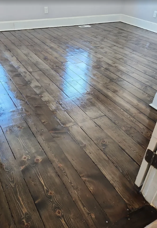 Empty room with weathered dark hardwood floors and white baseboards, lit by window reflection.