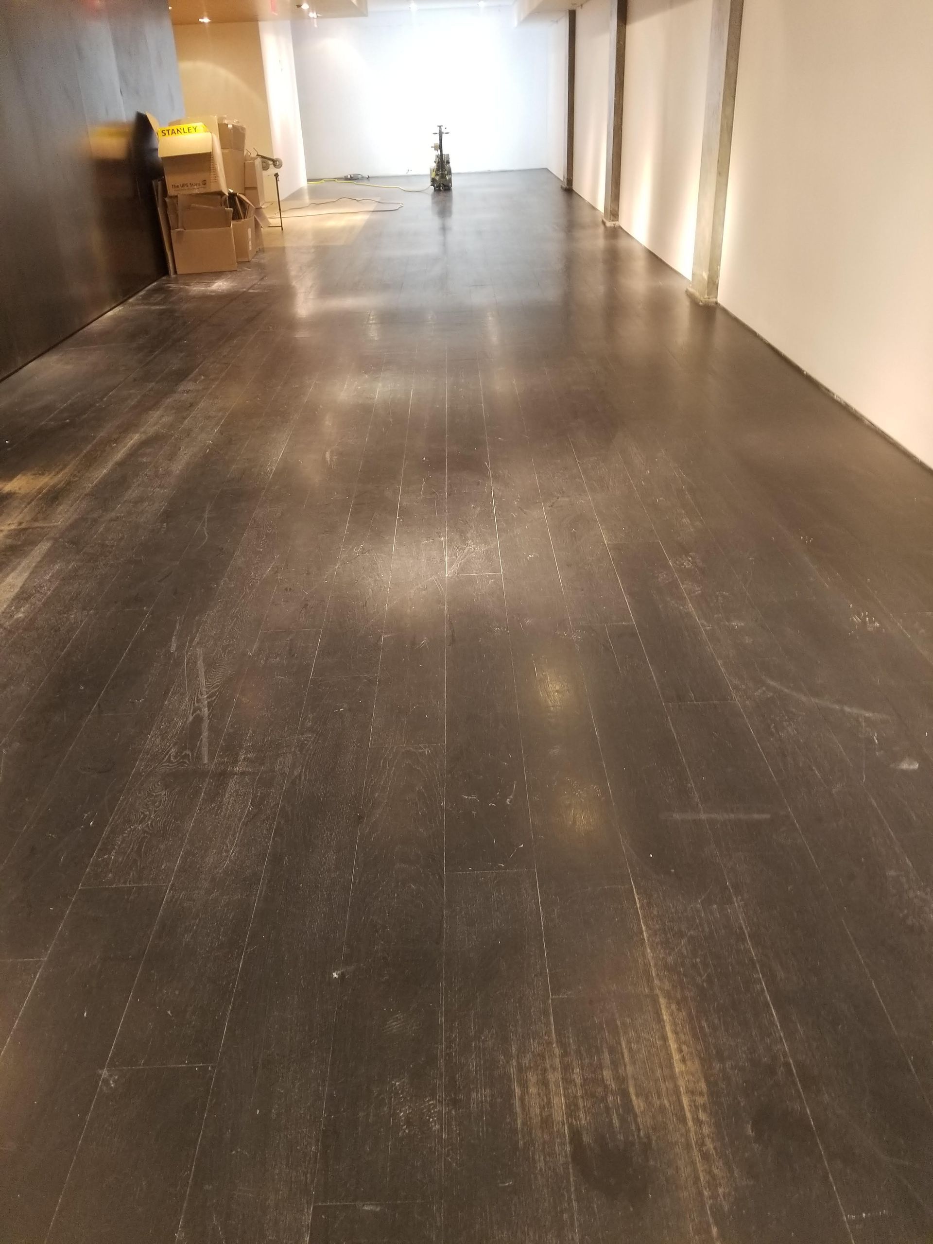 Empty gallery hallway with dark floor and white walls, lit by overhead lights.