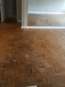 Empty room with parquet wood floor and gray walls, lit by daylight from a window.