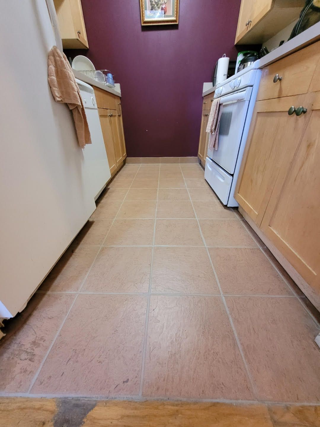 Narrow kitchen aisle with tan tile floor, wood cabinets, white stove, and deep red back wall.