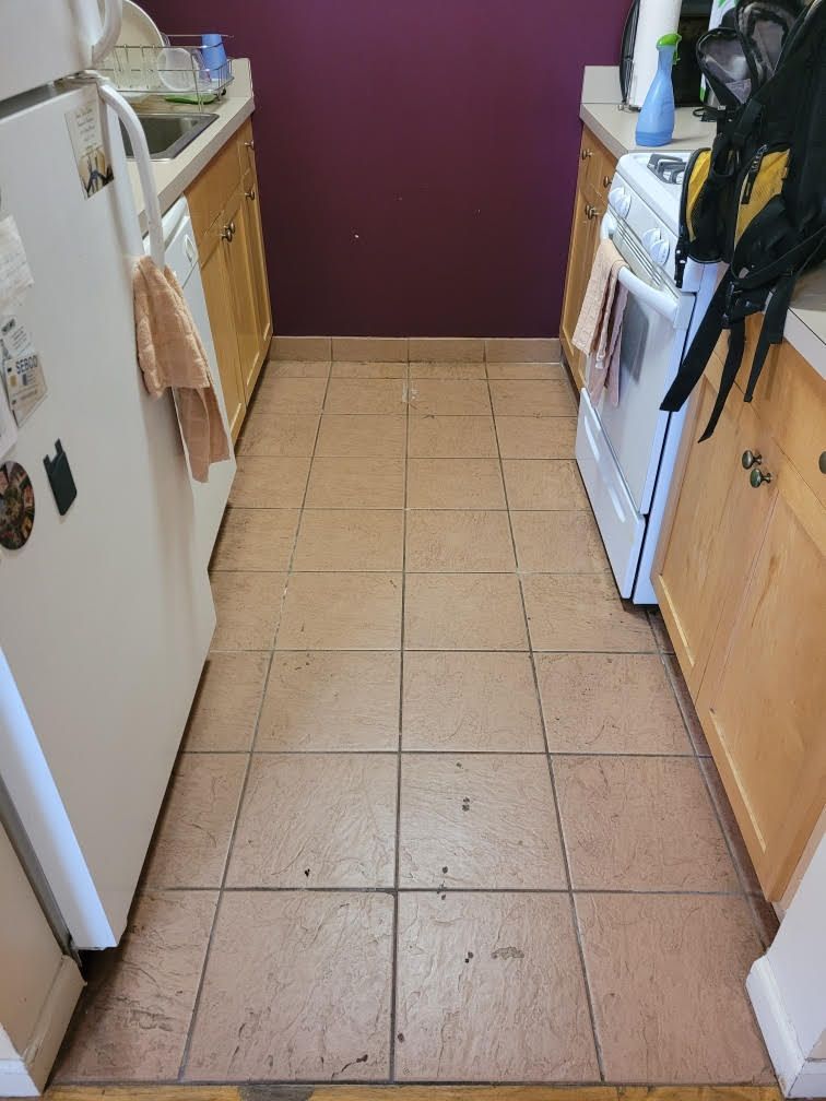 Narrow kitchen with beige tile floor, white appliances, and wood cabinets along both sides.