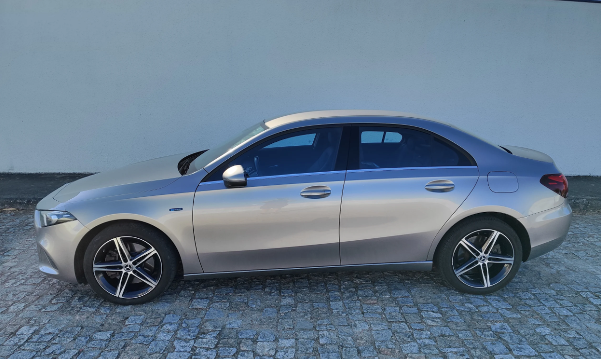 Sedã prateado estacionado em calçada de paralelepípedos ao lado de uma parede lisa.