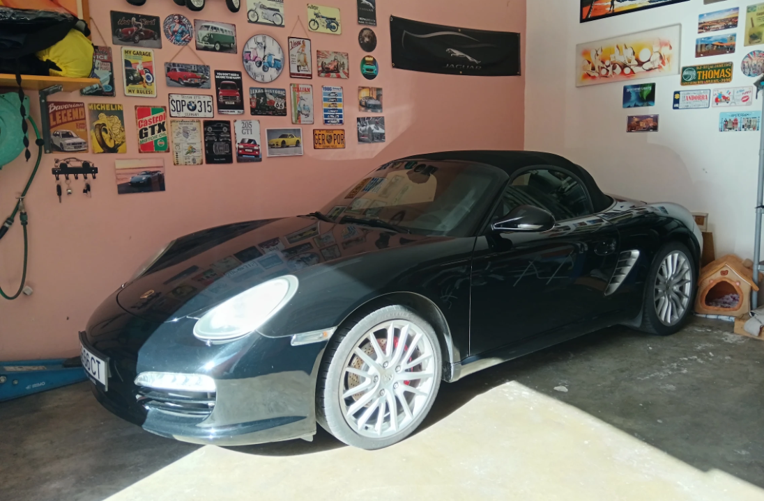 Carro desportivo preto estacionado dentro de uma garagem com paredes rosa e pôsteres na parede.