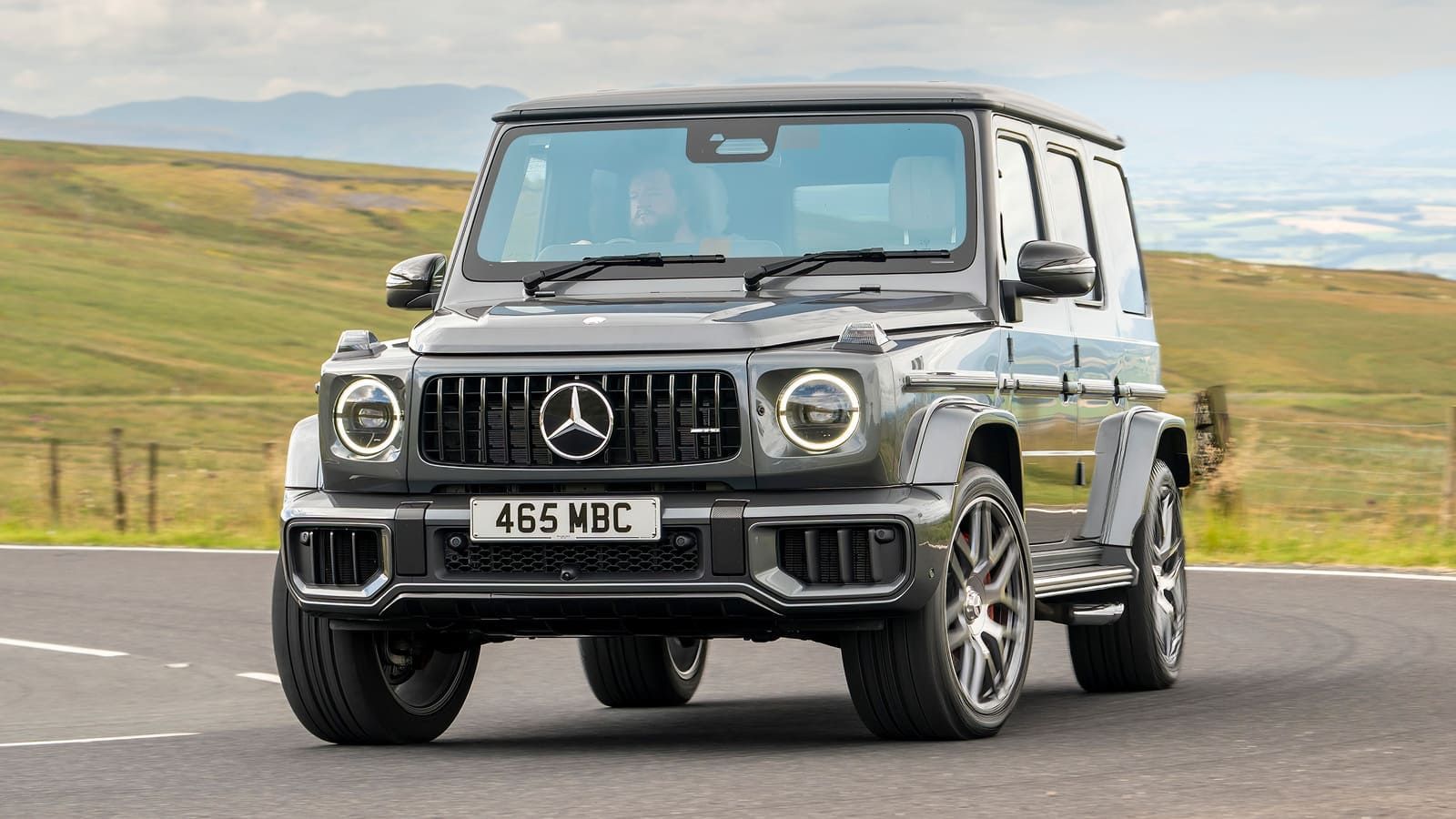 SUV Mercedes-Benz Classe G preta estacionada em uma estrada rural com colinas onduladas ao fundo.