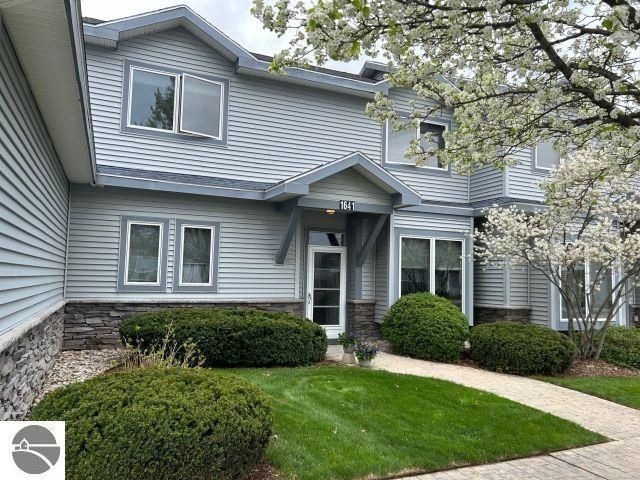 A large gray house with a lot of windows and bushes in front of it.