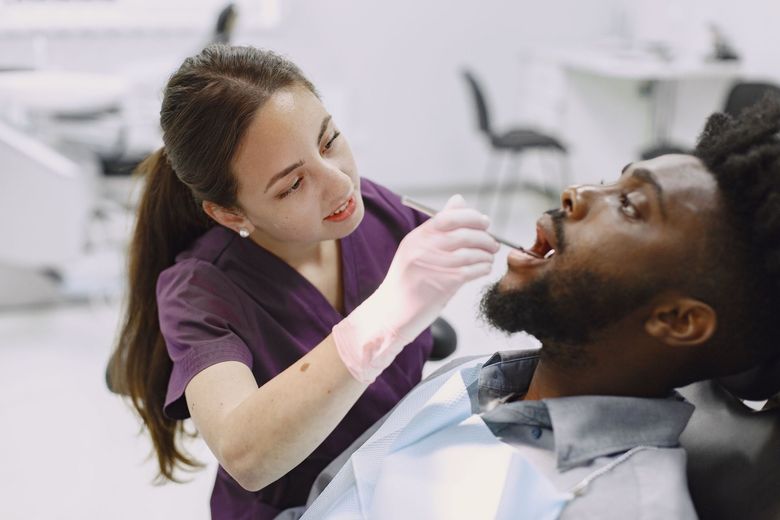 Dentist examining a patient’s mouth in a dental chair with a dental mirror and gloves