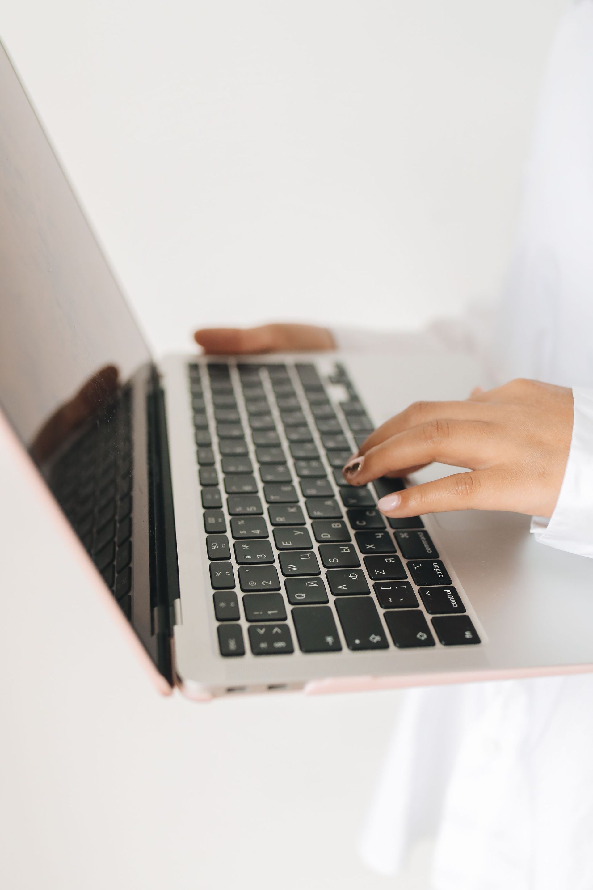 Hands typing on a silver laptop keyboard against a white background
