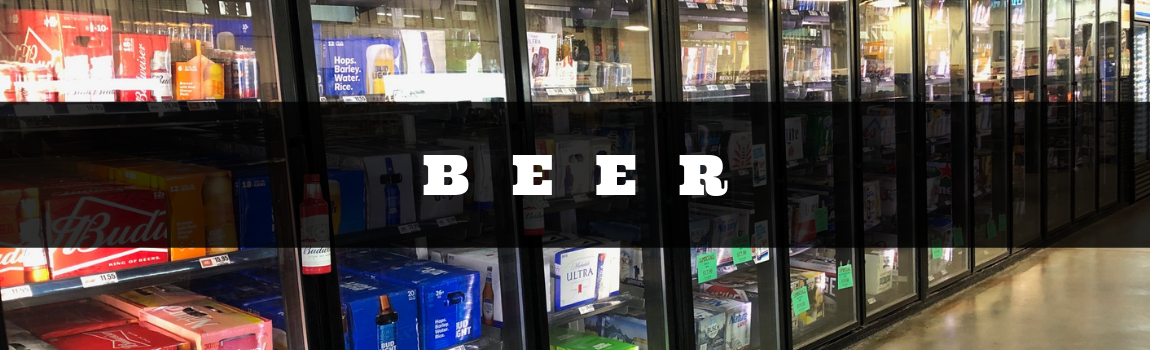 Beer display in a store cooler with bottles and cans behind glass doors