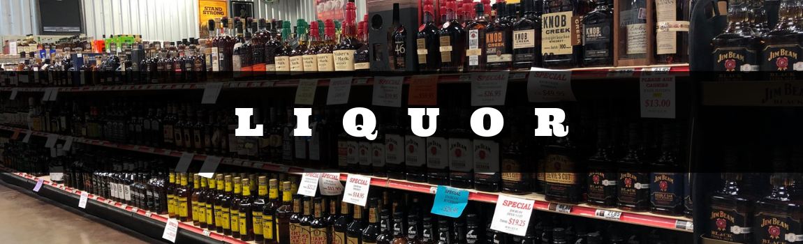Liquor store aisle with shelves of assorted bottles and a large “LIQUOR” sign overhead