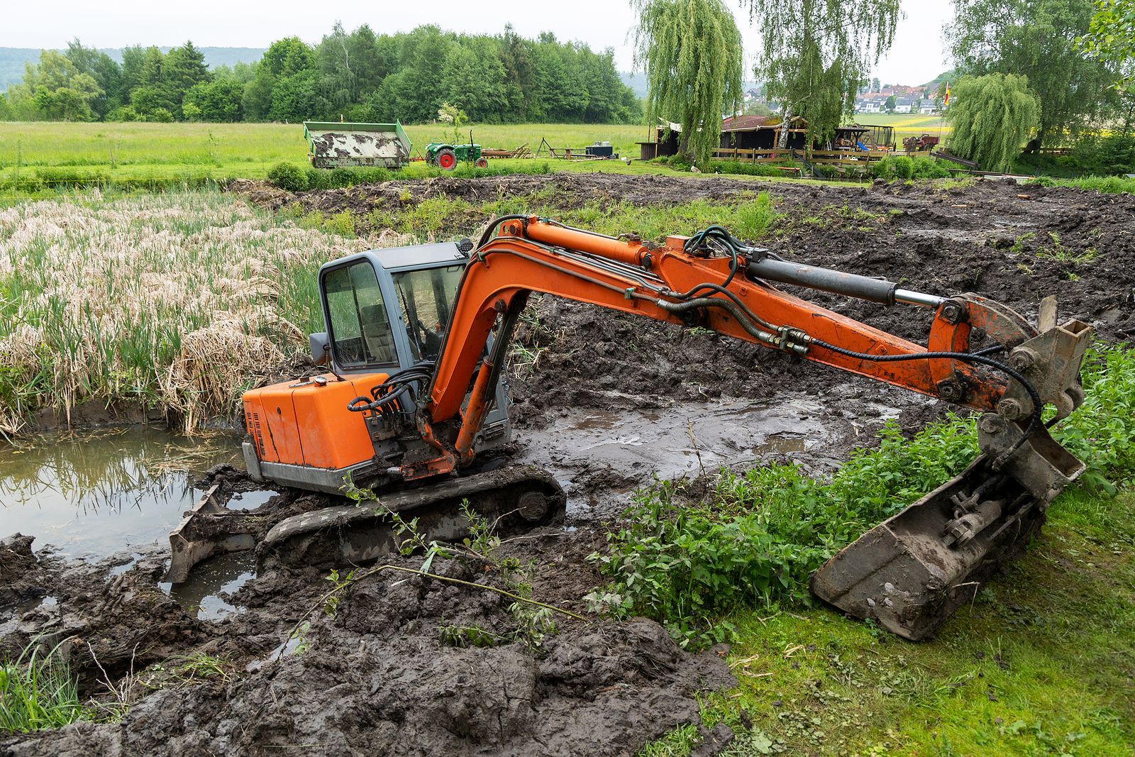 An orange excavator is digging a muddy field next to a river.