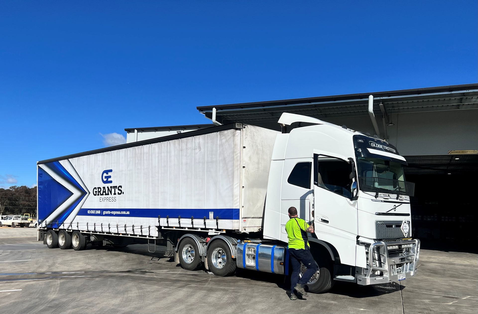 White Freightliner Box Truck Parked by Warehouse, With a Worker in a Yellow Vest Beside the Cab — Grants Express in Eastern Creek, NSW