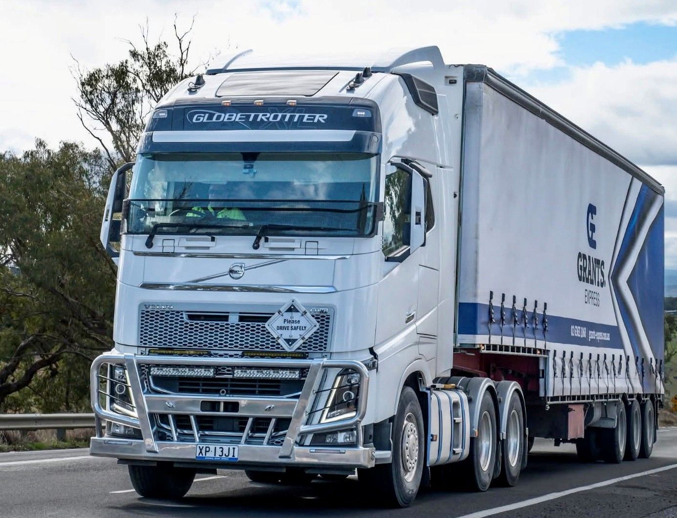 White semi-truck driving on a road, with a silver trailer and blue accents under a cloudy sky — Grants Express in Orange, NSW
