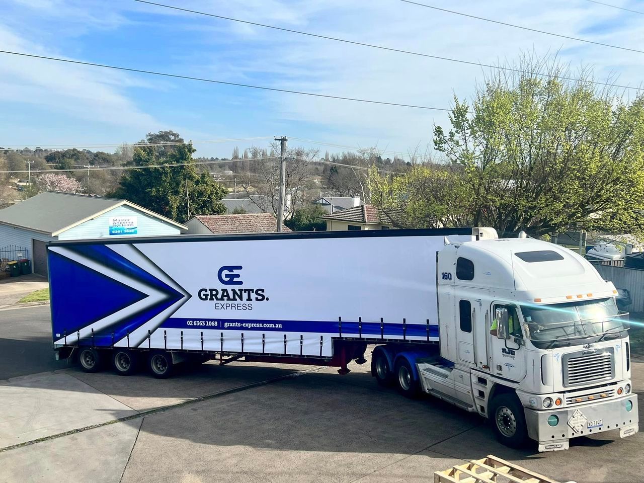 White Semi-truck Trailer With Blue “GRANTS” Logo Parked Near Buildings Under a Clear Sky — Grants Express in Parkes, NSW