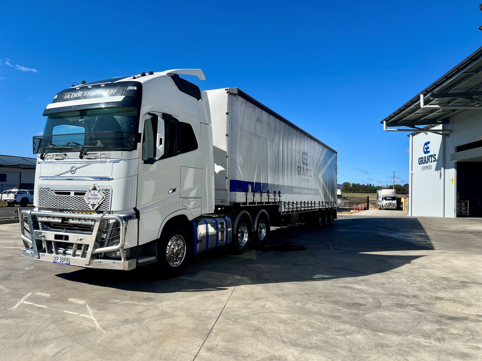 White Semi-truck With a Silver Trailer Parked on a Concrete Lot Under a Clear Blue Sky — Grants Express in Eastern Creek, NSW