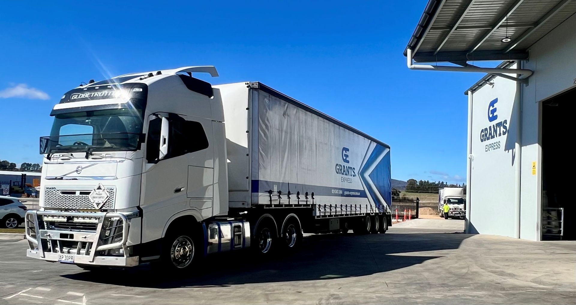 White semi-truck with a blue trailer parked beside a warehouse under a clear blue sky — Grants Express in Orange, NSW
