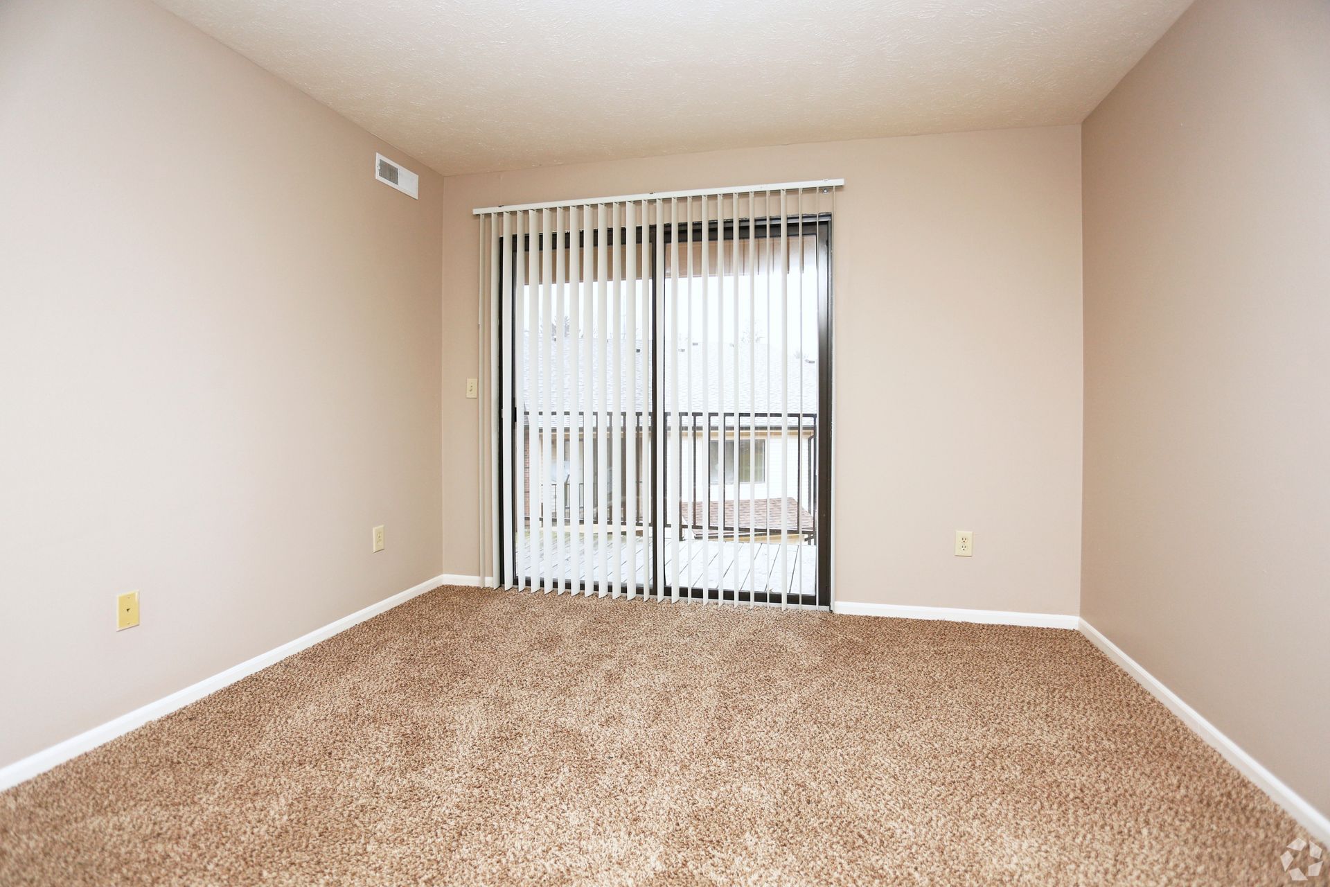 An empty living room with a sliding glass door and blinds.