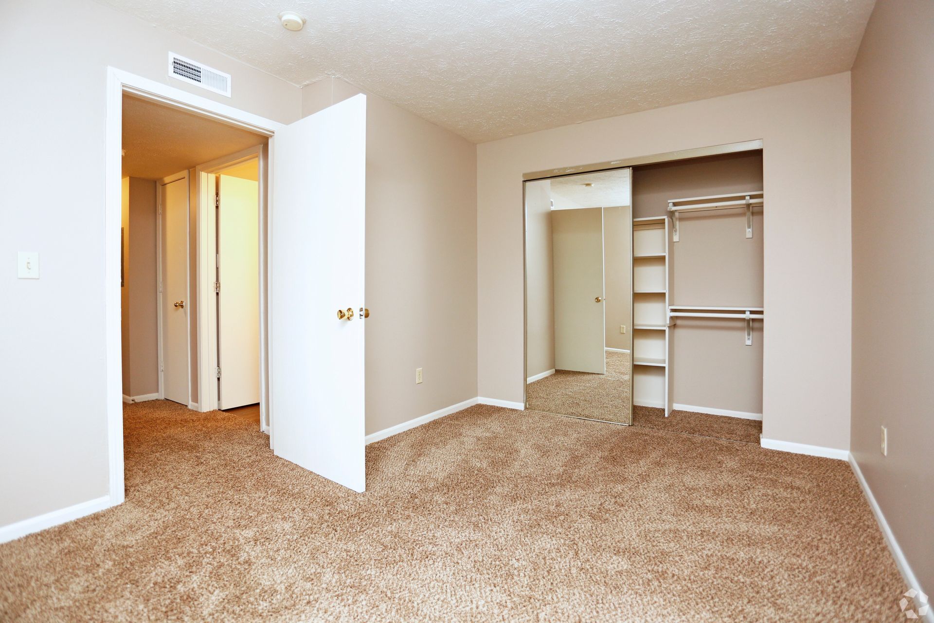 An empty bedroom with a walk in closet and a large mirror.