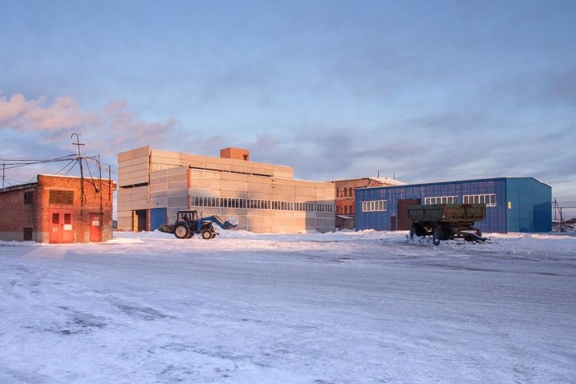 Snowy industrial yard with large buildings and vehicles at sunset