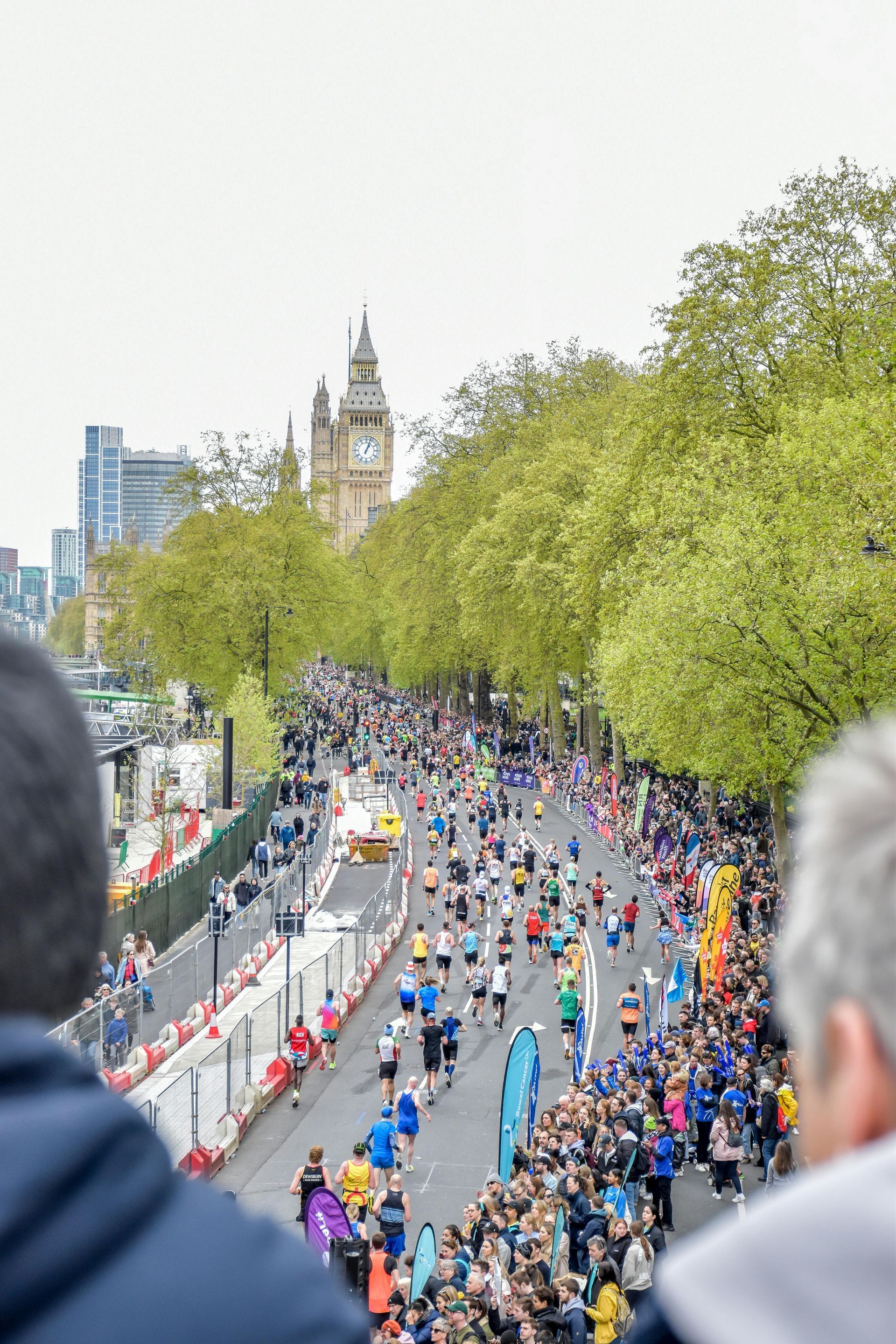 Runners in a marathon on a London street, Big Ben in background, lined by spectators and trees.