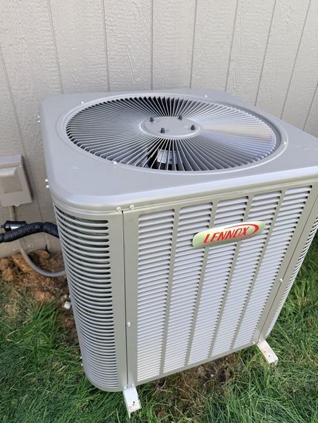 Outdoor Lennox air conditioner unit beside a house wall on a grassy strip.