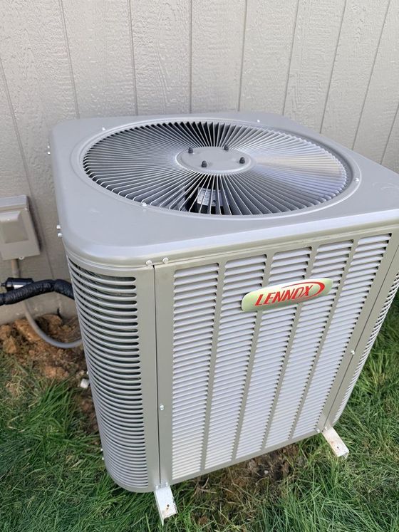 Outdoor Lennox air conditioner unit beside a house wall on a grassy strip.