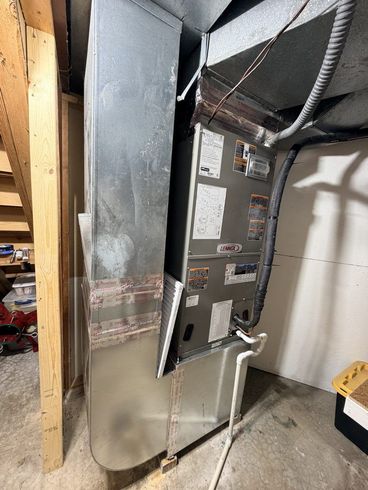 Metal HVAC furnace in a utility room with exposed ducts and wiring