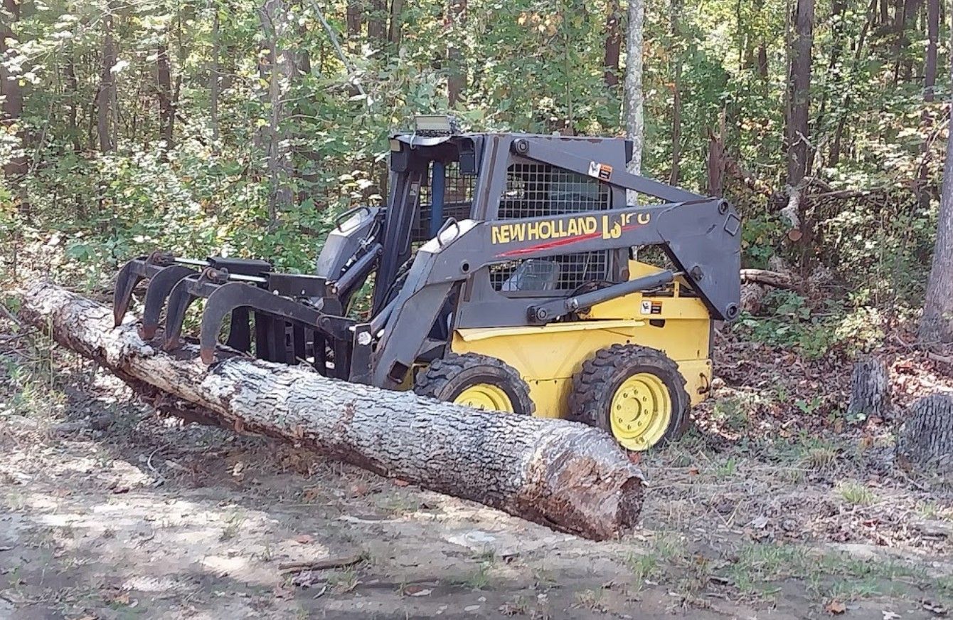 A new holland skid steer is cutting a log in the woods.