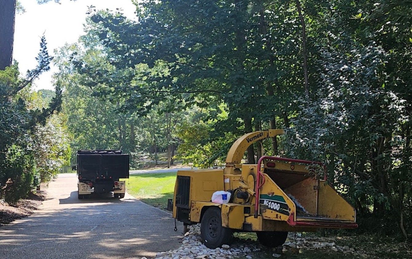 A yellow tree chipper is parked on the side of a dirt road.