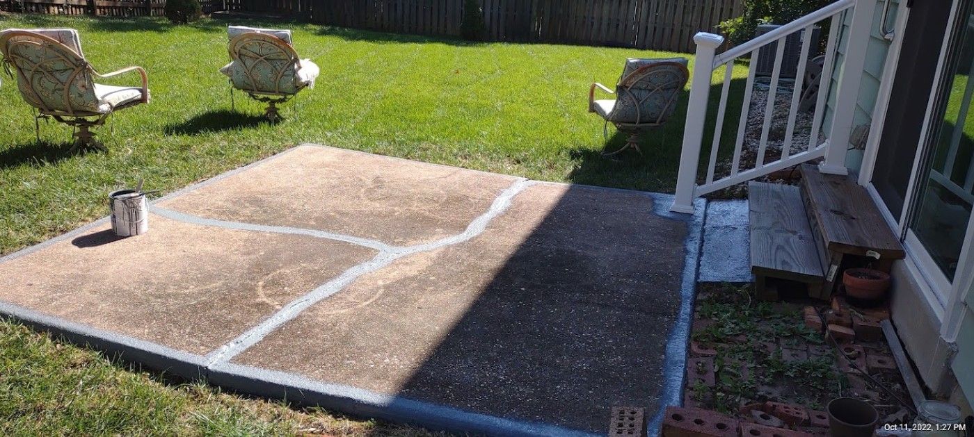 A concrete patio in a backyard with chairs and a white railing.