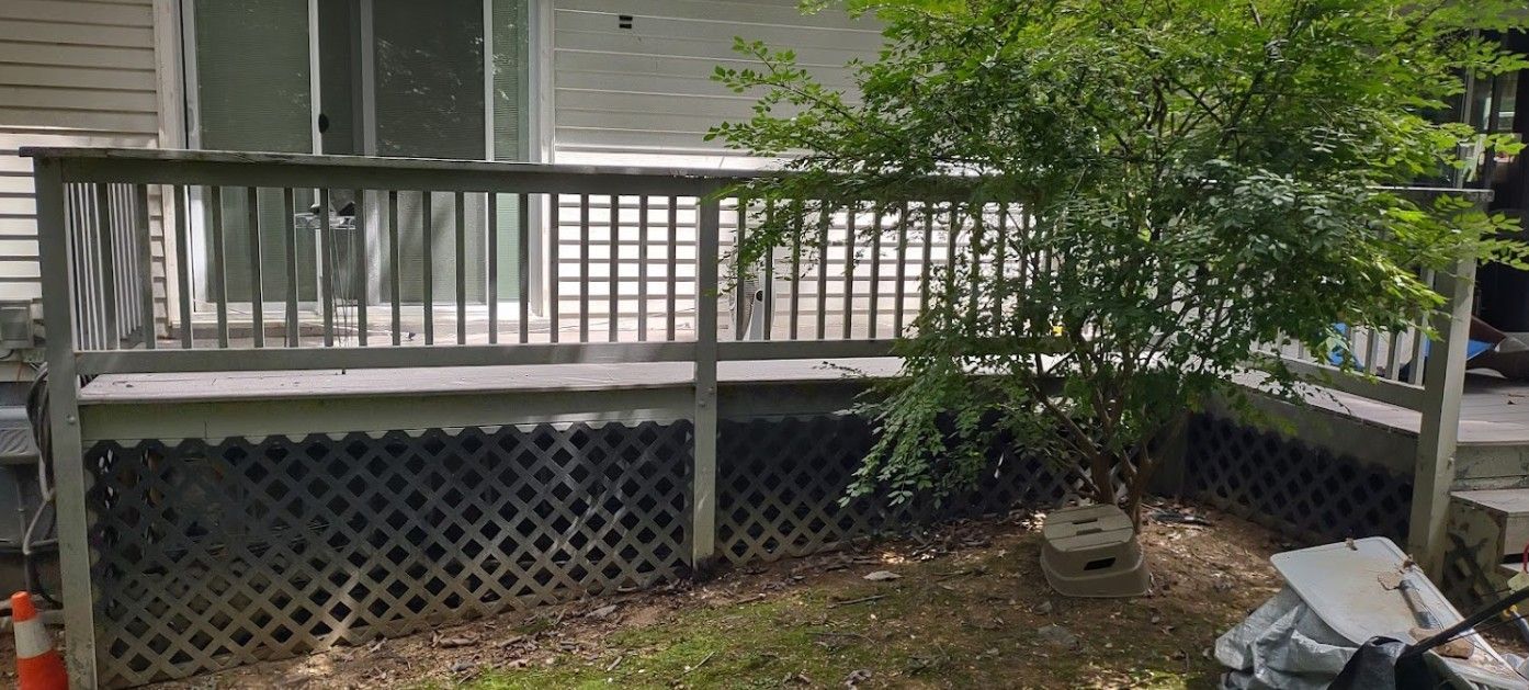 A wooden deck with a fence and a tree in front of a house.