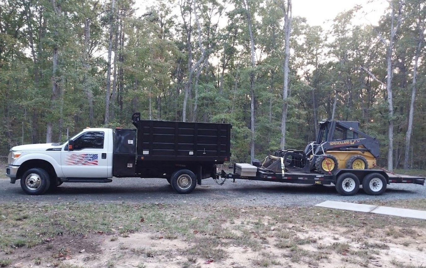 A dump truck is towing a small tractor on a trailer.