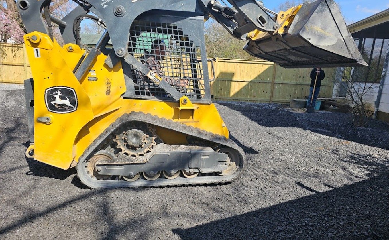 A yellow and black john deere skid steer is loading gravel into a bucket.