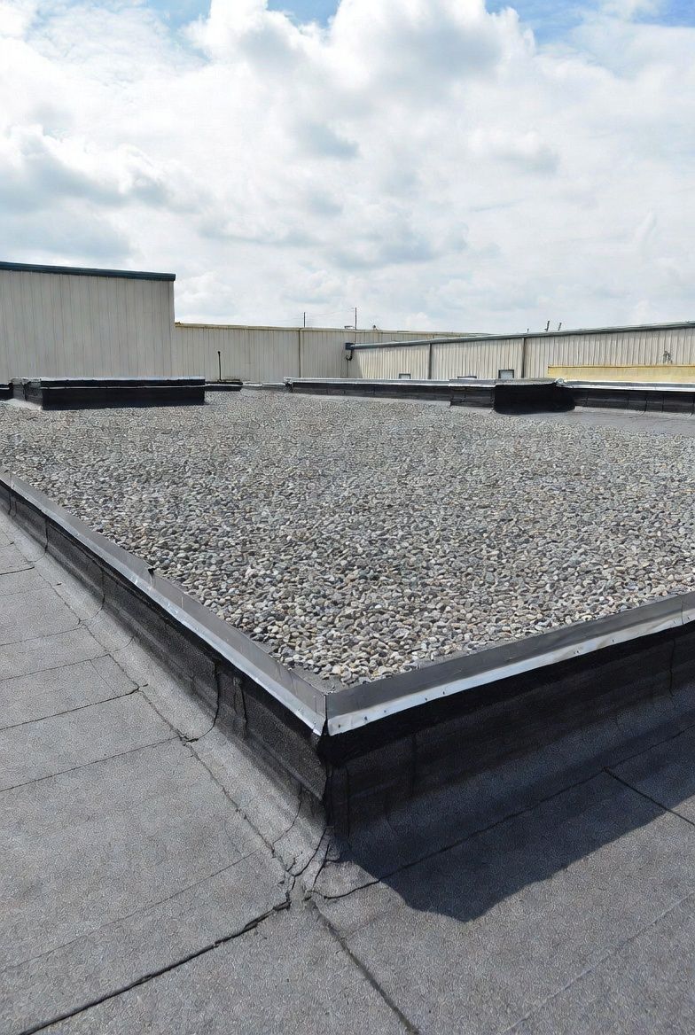 Flat roof covered in gravel, with a black border, against a cloudy sky.
