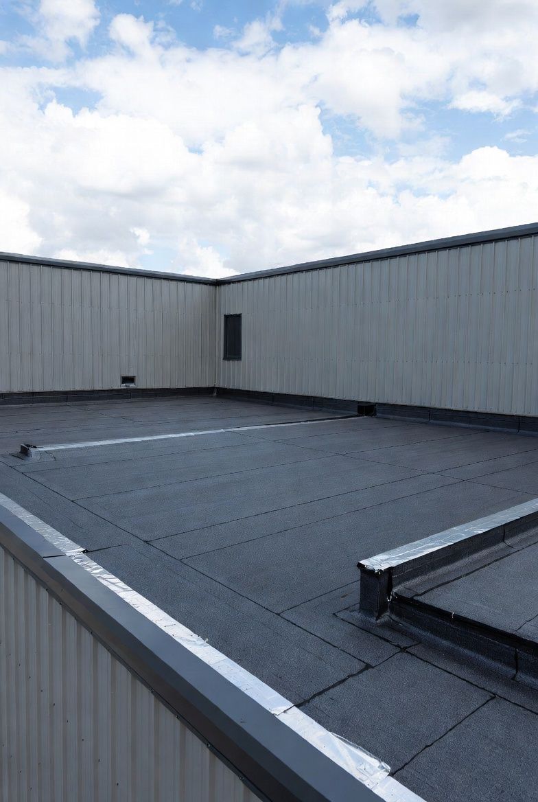 Flat, black rooftop with a light gray building and a partly cloudy sky.